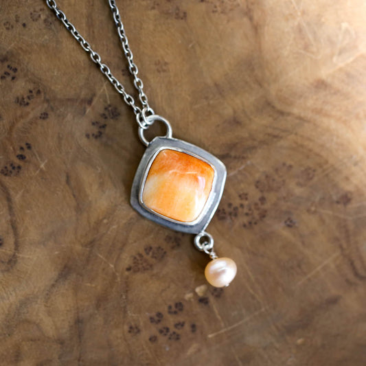 May include: A silver necklace with a square pendant featuring an orange gemstone and a single pearl drop.