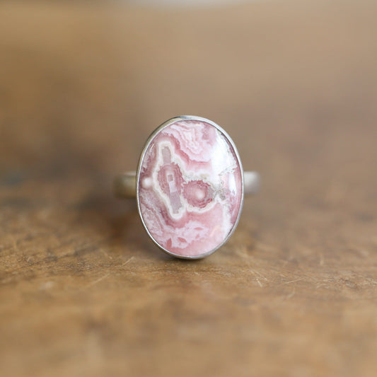 May include: A silver ring with a pink and white oval shaped stone set in the center.
