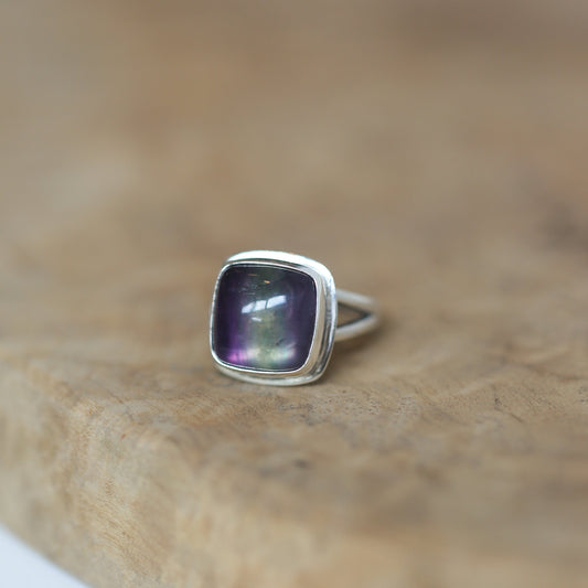 May include: A silver ring with a square-shaped, iridescent purple gemstone.