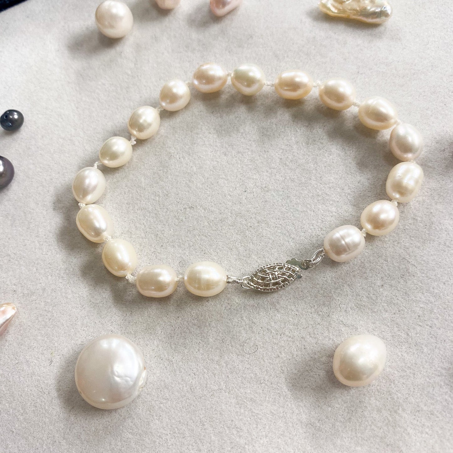 A freshwater pearl bracelet with irregular baroque pearls and a silver-toned leaf clasp, displayed on a light gray textured surface with loose pearls nearby.