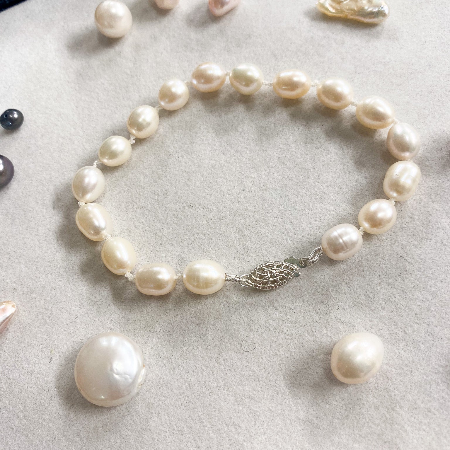 A freshwater pearl bracelet with irregular baroque pearls and a silver-toned leaf clasp, displayed on a light gray textured surface with loose pearls nearby.