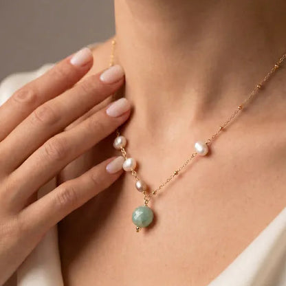 Necklace with pearls and a green gemstone worn by a person, with a neutral background.