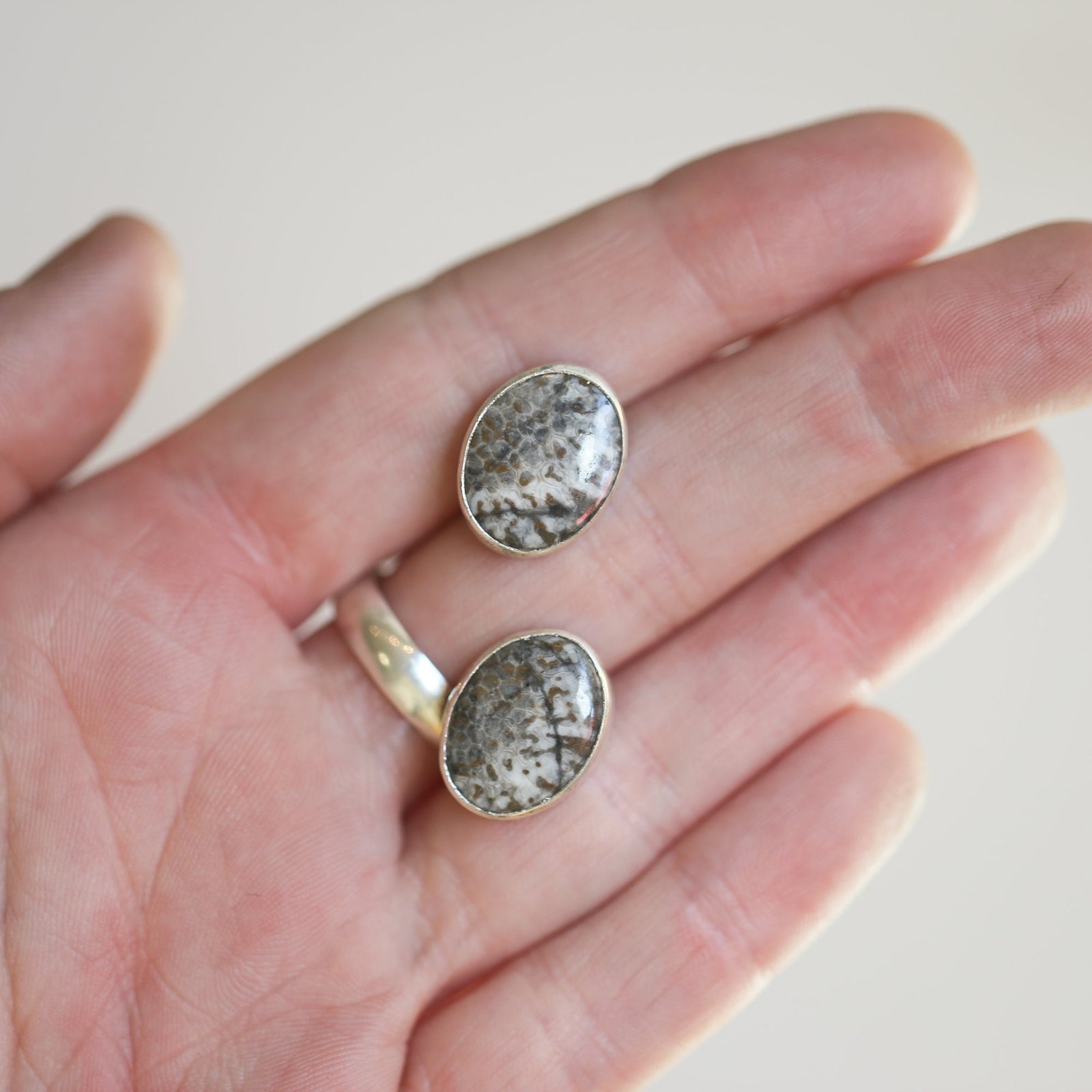May include: Two oval-shaped earrings with silver settings and a gray and white stone inlay.