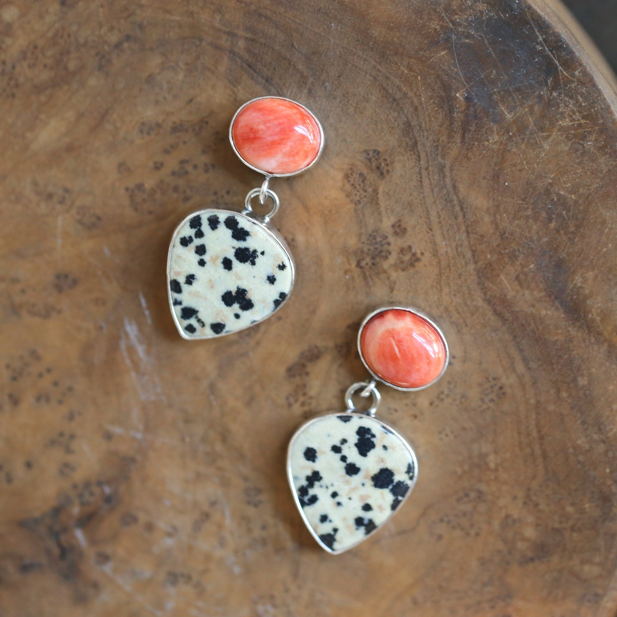 May include: A pair of dangle earrings with a teardrop shaped dalmatian jasper stone and a round orange coral stone on each earring.