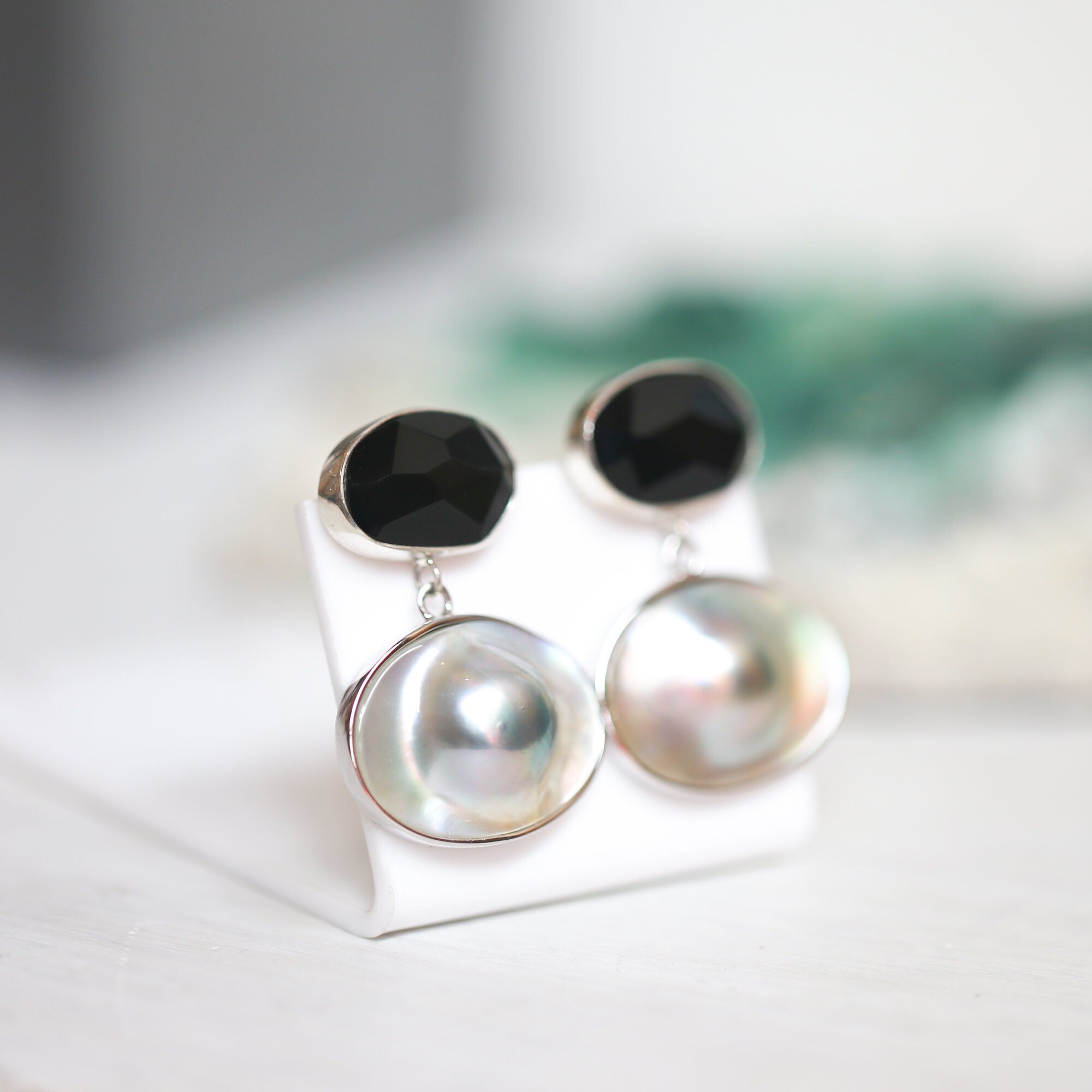 May include: A pair of silver earrings with black and white gemstone accents. The earrings feature a black gemstone on top and a white pearl-like gemstone on the bottom.
