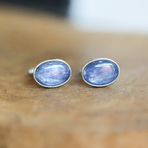 May include: Two silver cufflinks with oval-shaped blue stones. The stones have a shimmery, iridescent finish.