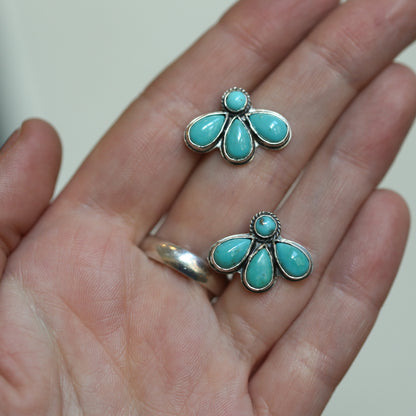 May include: Two silver earrings with turquoise stones. Each earring has five turquoise stones in a flower shape.