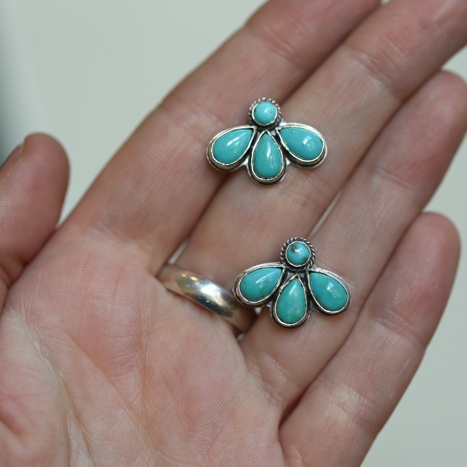 May include: Two silver earrings with turquoise stones. Each earring has five turquoise stones in a flower shape.