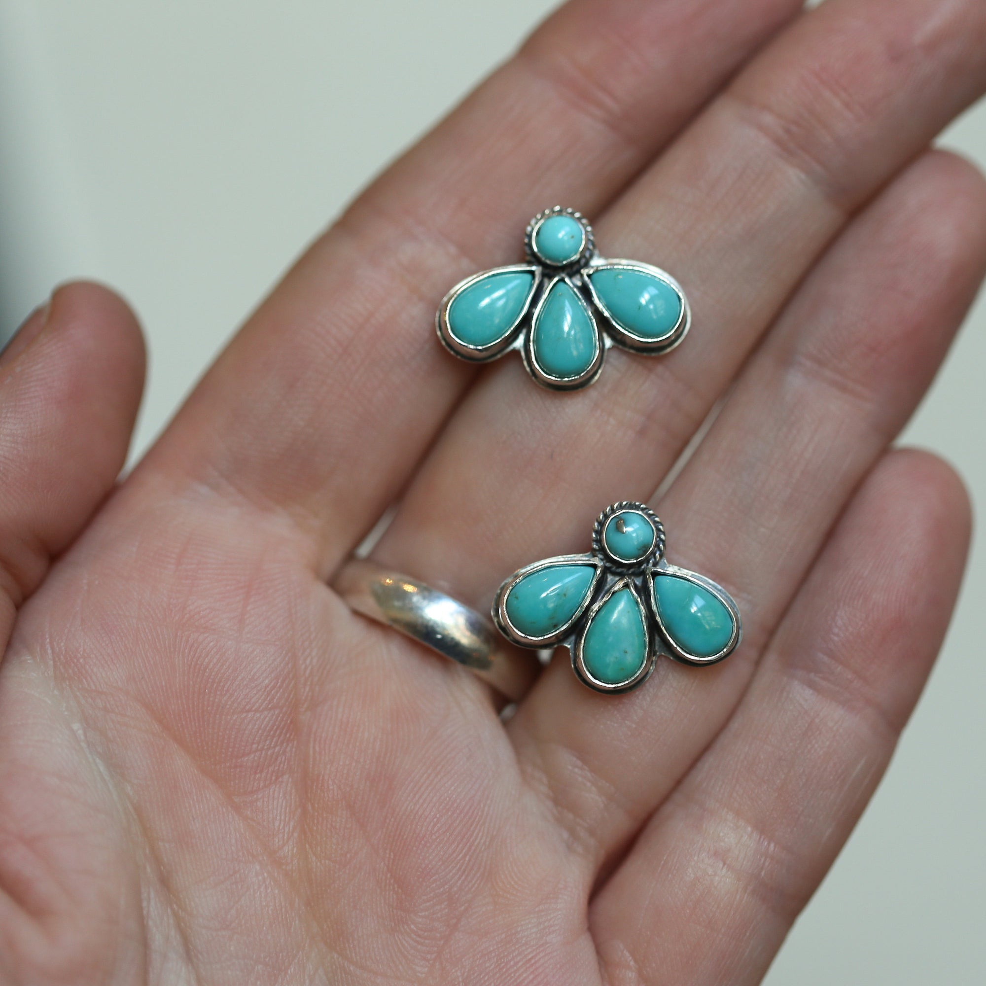 May include: Two silver earrings with turquoise stones. Each earring has five turquoise stones in a flower shape.
