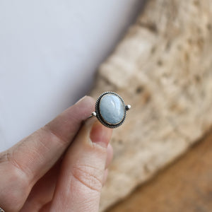 May include: A silver ring with an oval shaped light blue gemstone set in a silver bezel setting.