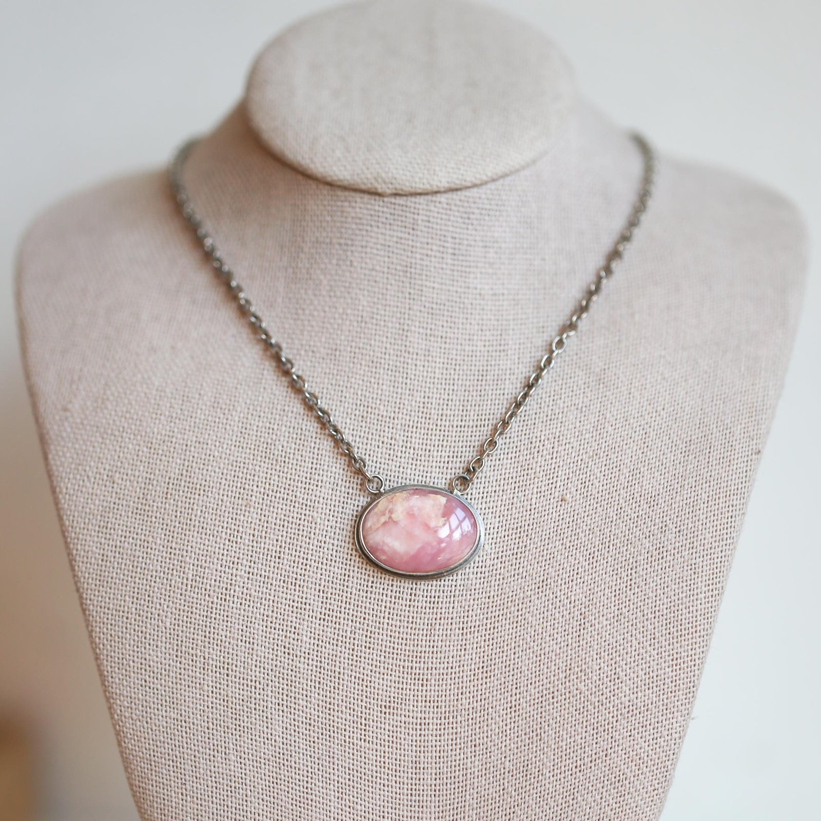 May include: A silver chain necklace with a pink oval pendant