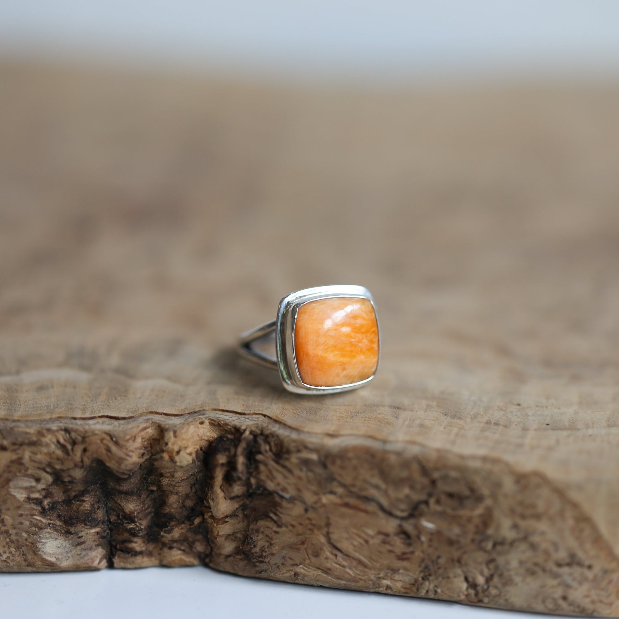 May include: A silver ring with a square orange gemstone