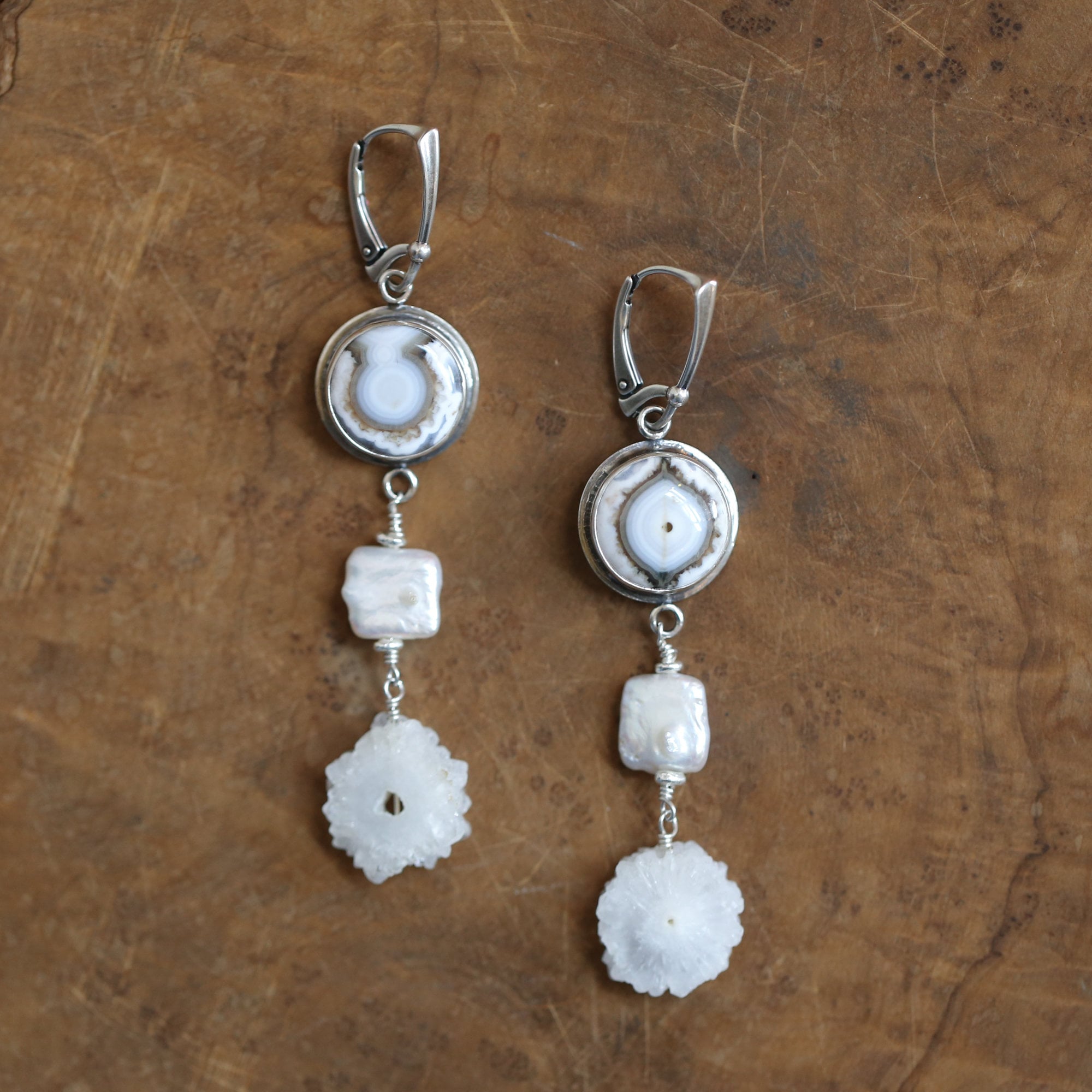 May include: A pair of silver earrings with white agate and pearl accents. Each earring features a round white agate stone with a silver setting, a square pearl bead, and a flower-shaped crystal bead.