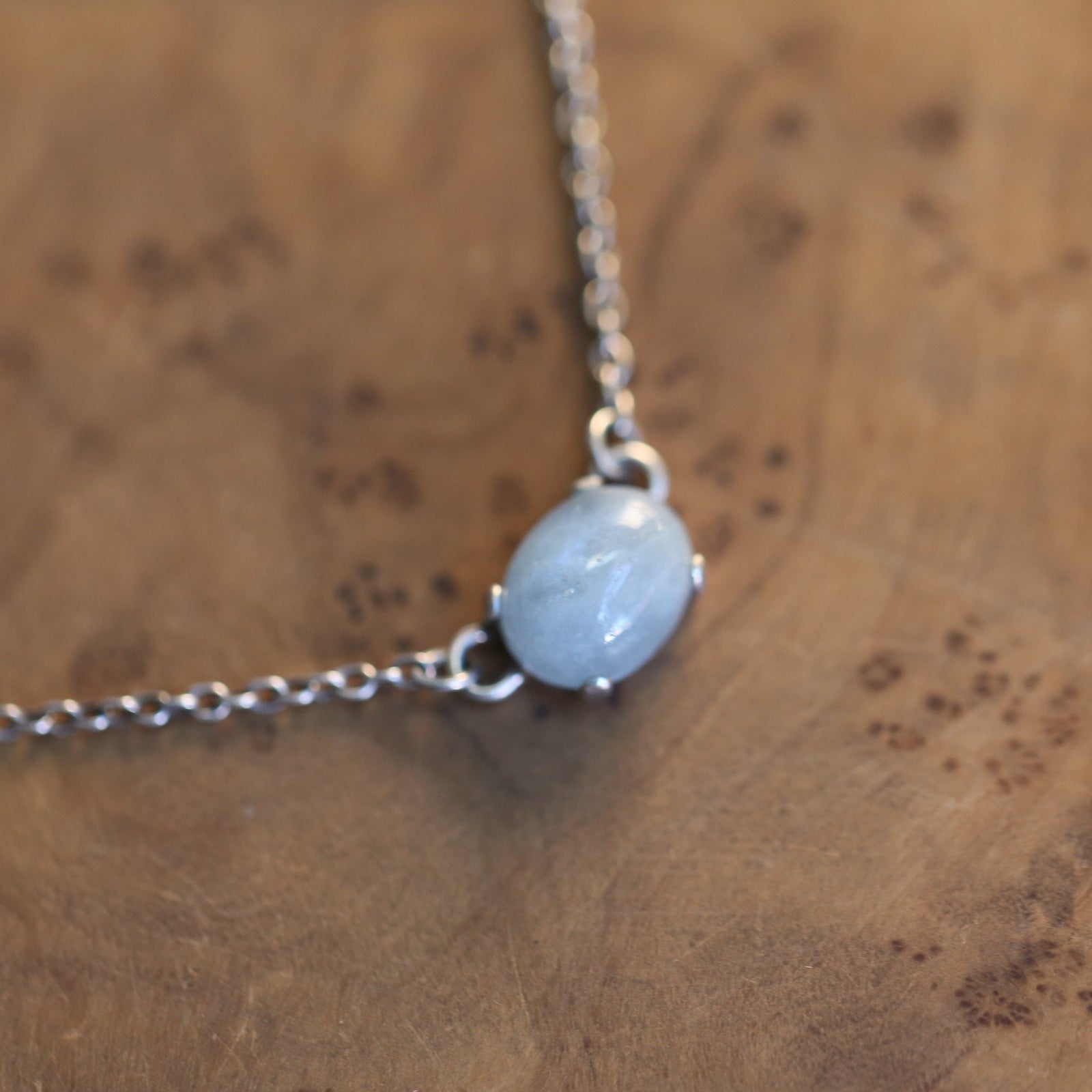 May include: A silver chain necklace with a light blue oval gemstone pendant.