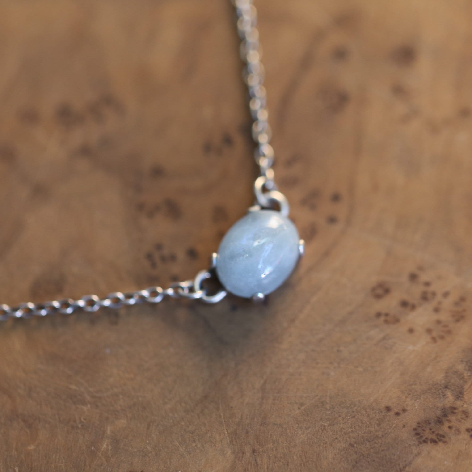 May include: A silver chain necklace with a light blue oval gemstone pendant.