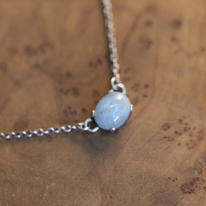 May include: A silver chain necklace with a light blue oval gemstone pendant.