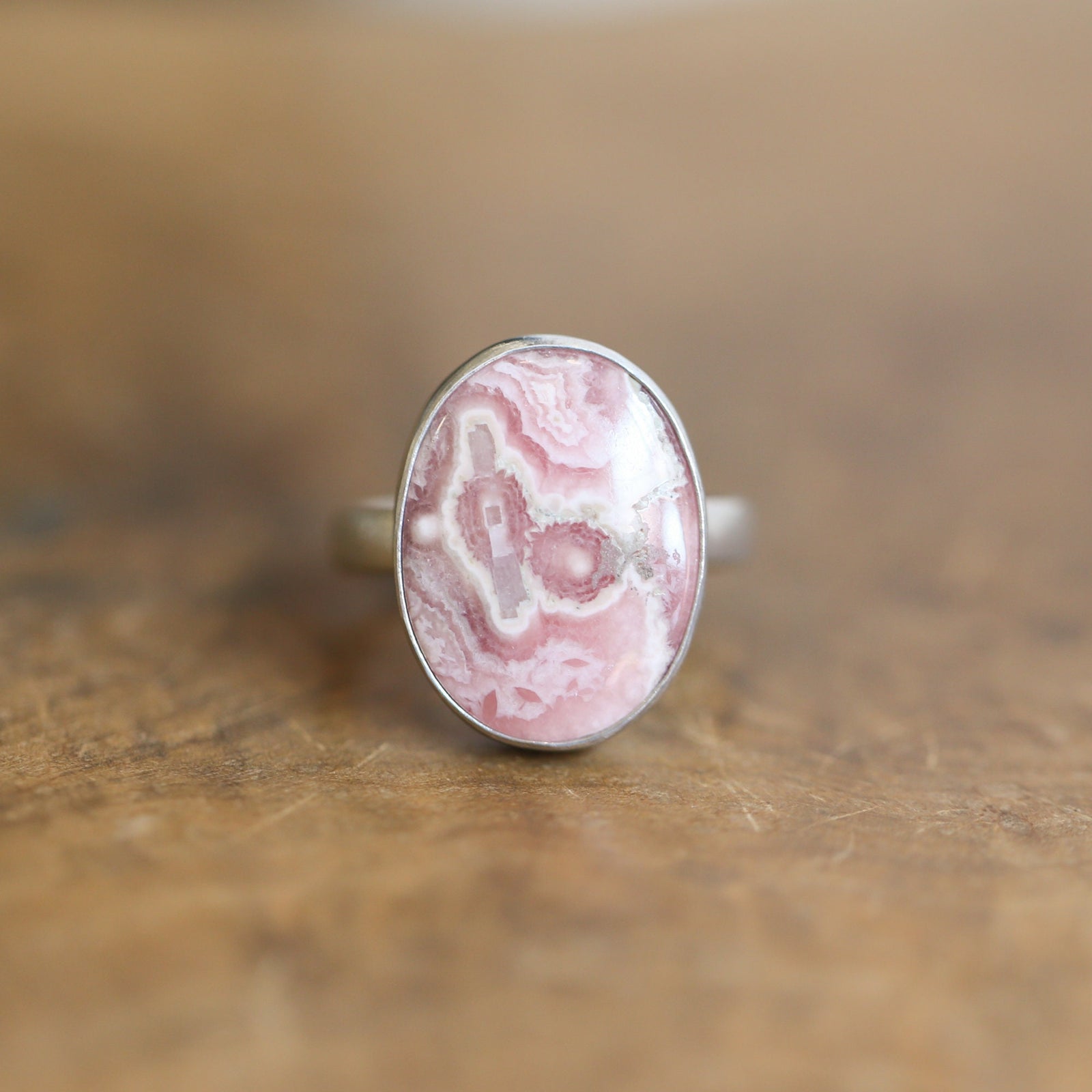 May include: A silver ring with a pink and white oval shaped stone set in the center.