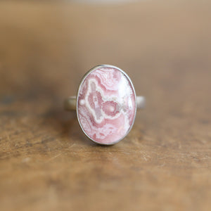 May include: A silver ring with a pink and white oval shaped stone set in the center.