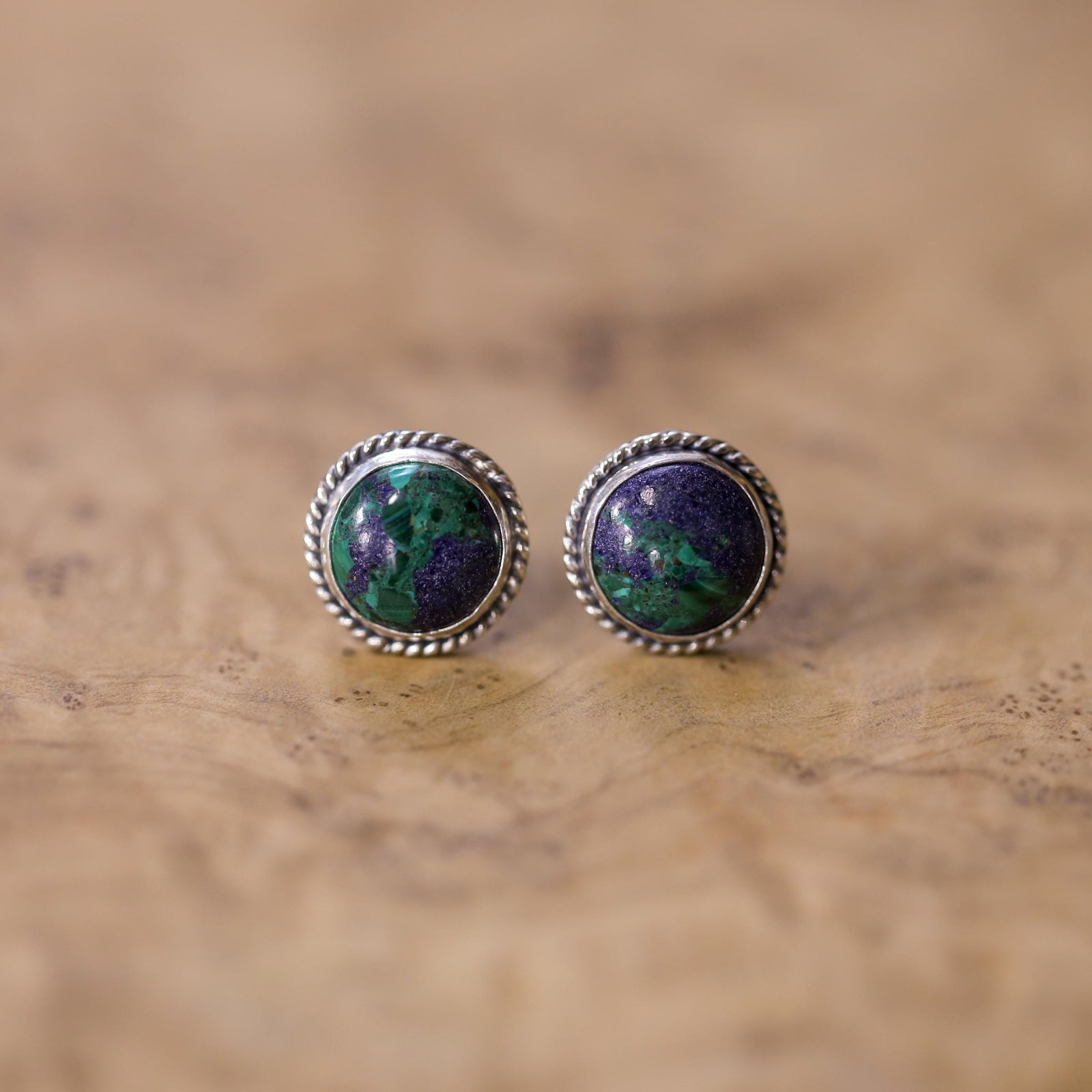 May include: A pair of silver earrings with green and purple malachite stone cabochons. The earrings have a round shape with a rope-like border.