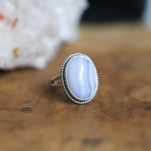 May include: A silver ring with a light blue agate oval gemstone set in a rope-like border.
