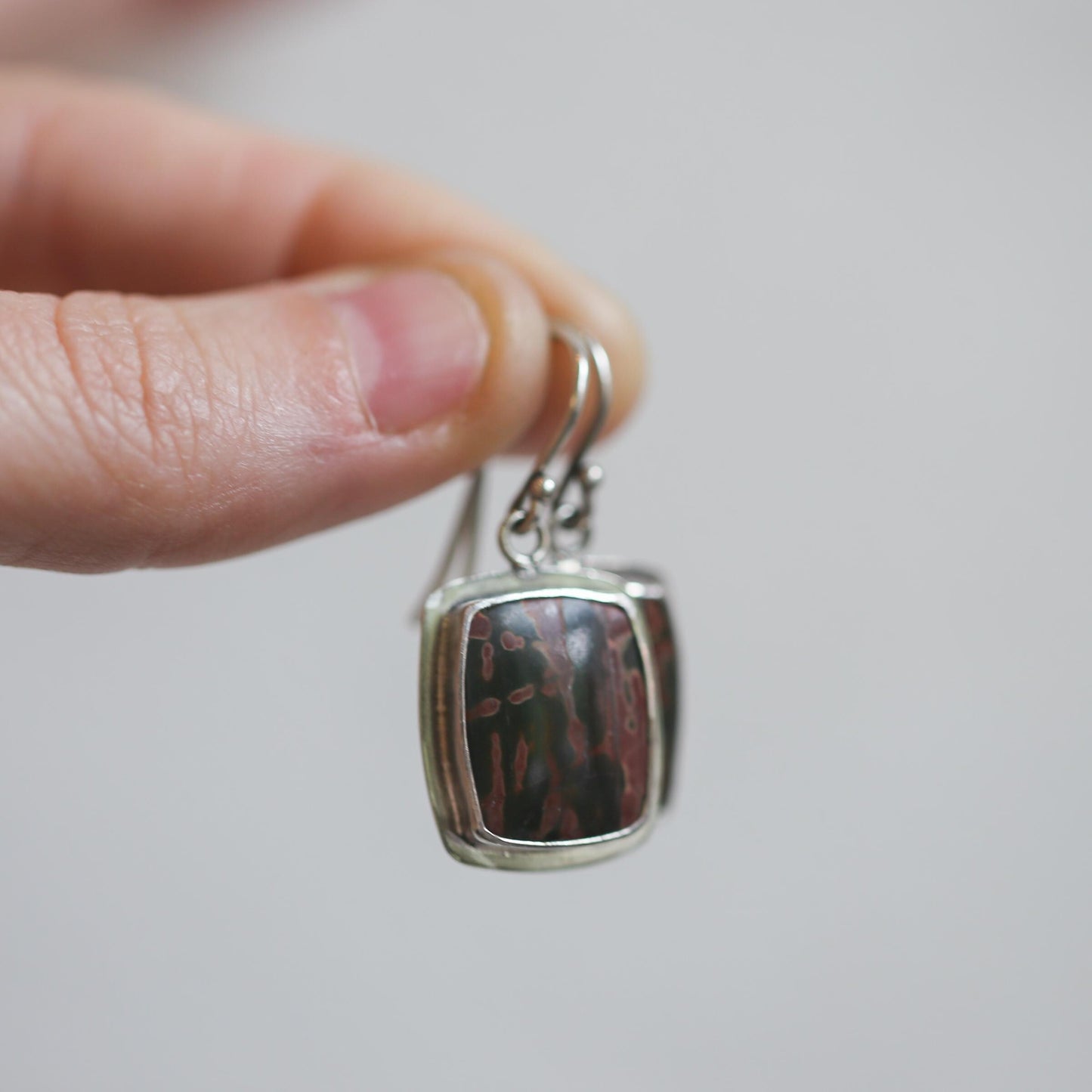 May include: A pair of silver earrings with a rectangular shaped stone set in the center. The stone is a dark brown color with a mottled pattern.