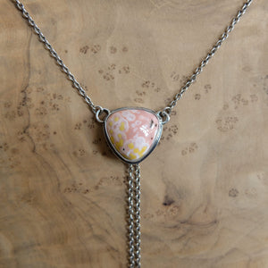 May include: A silver necklace featuring a triangular pendant with a pink and yellow stone. The stone has a unique pattern and is set in a silver bezel. The necklace chain is delicate, and a silver chain dangles from the bottom of the pendant.
