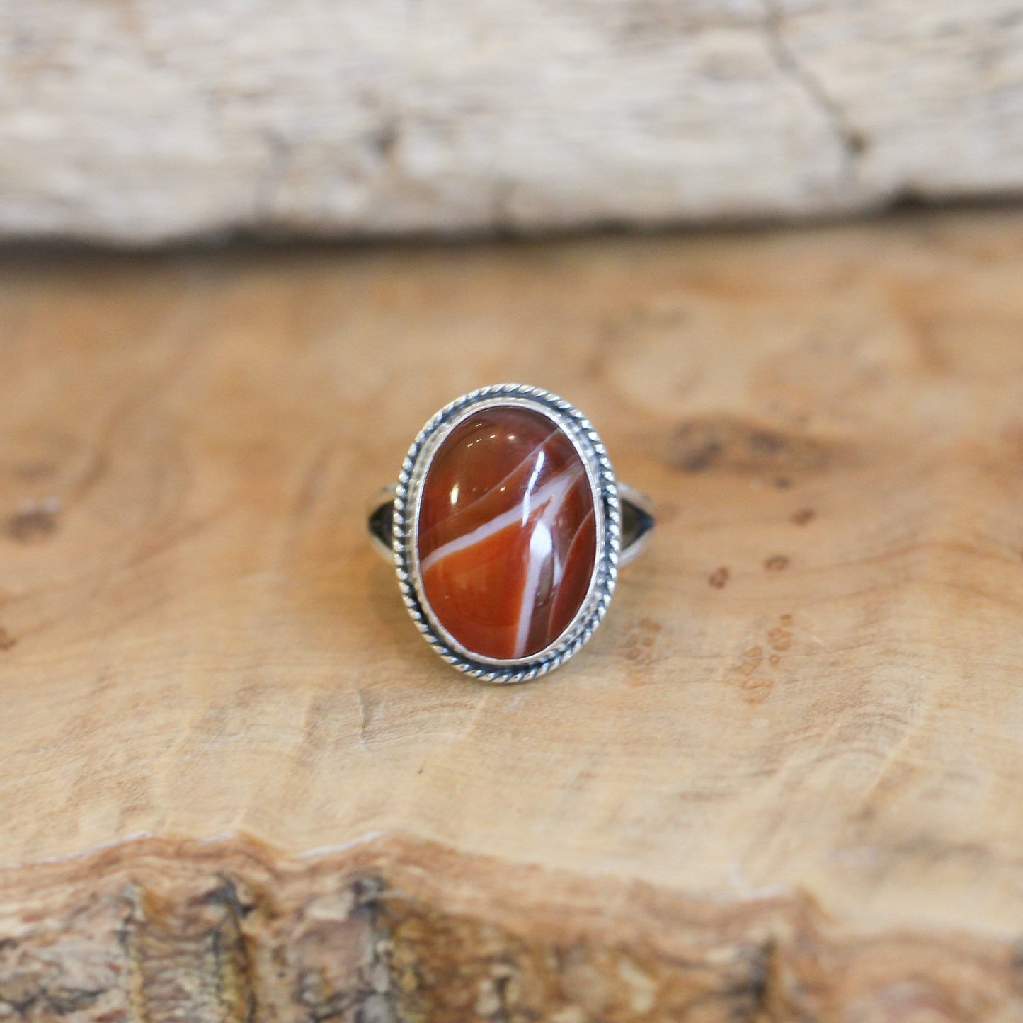 May include: A silver ring with an oval shaped red and white agate stone set in the center. The ring has a rope-like design around the edge of the setting.