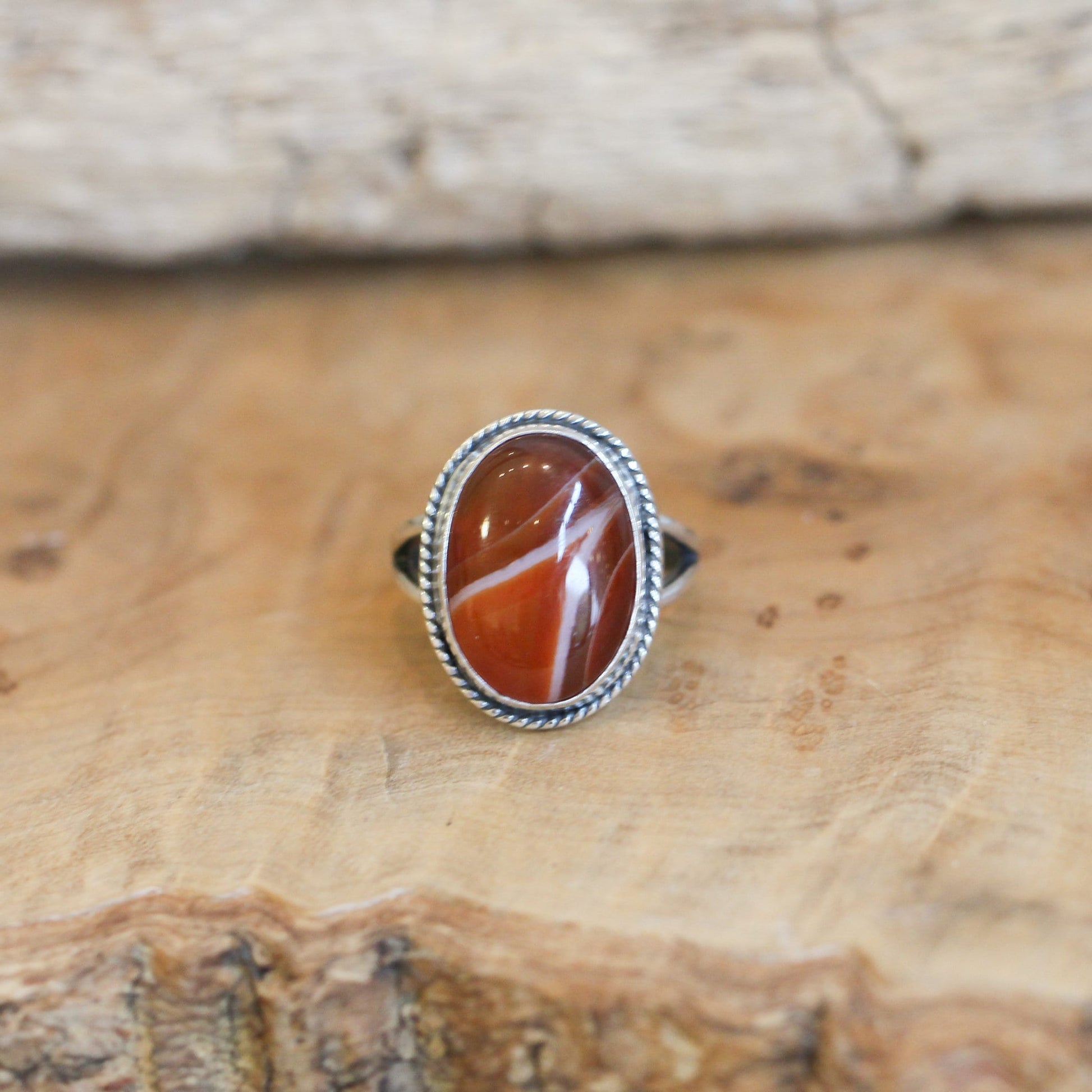 May include: A silver ring with an oval shaped red and white agate stone set in the center. The ring has a rope-like design around the edge of the setting.