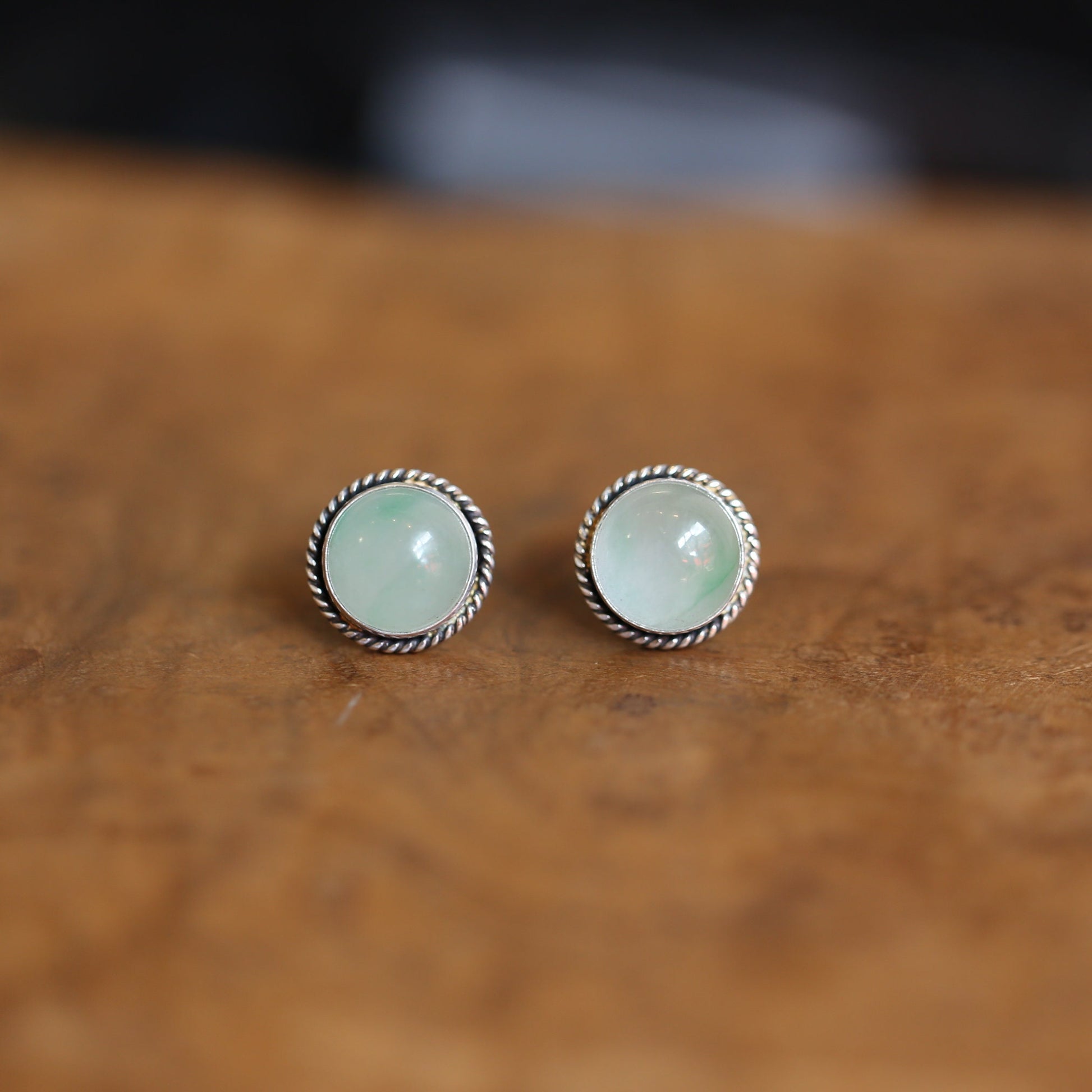 May include: A pair of silver earrings with a light green stone set in each. The stones are round and have a slightly cloudy appearance.