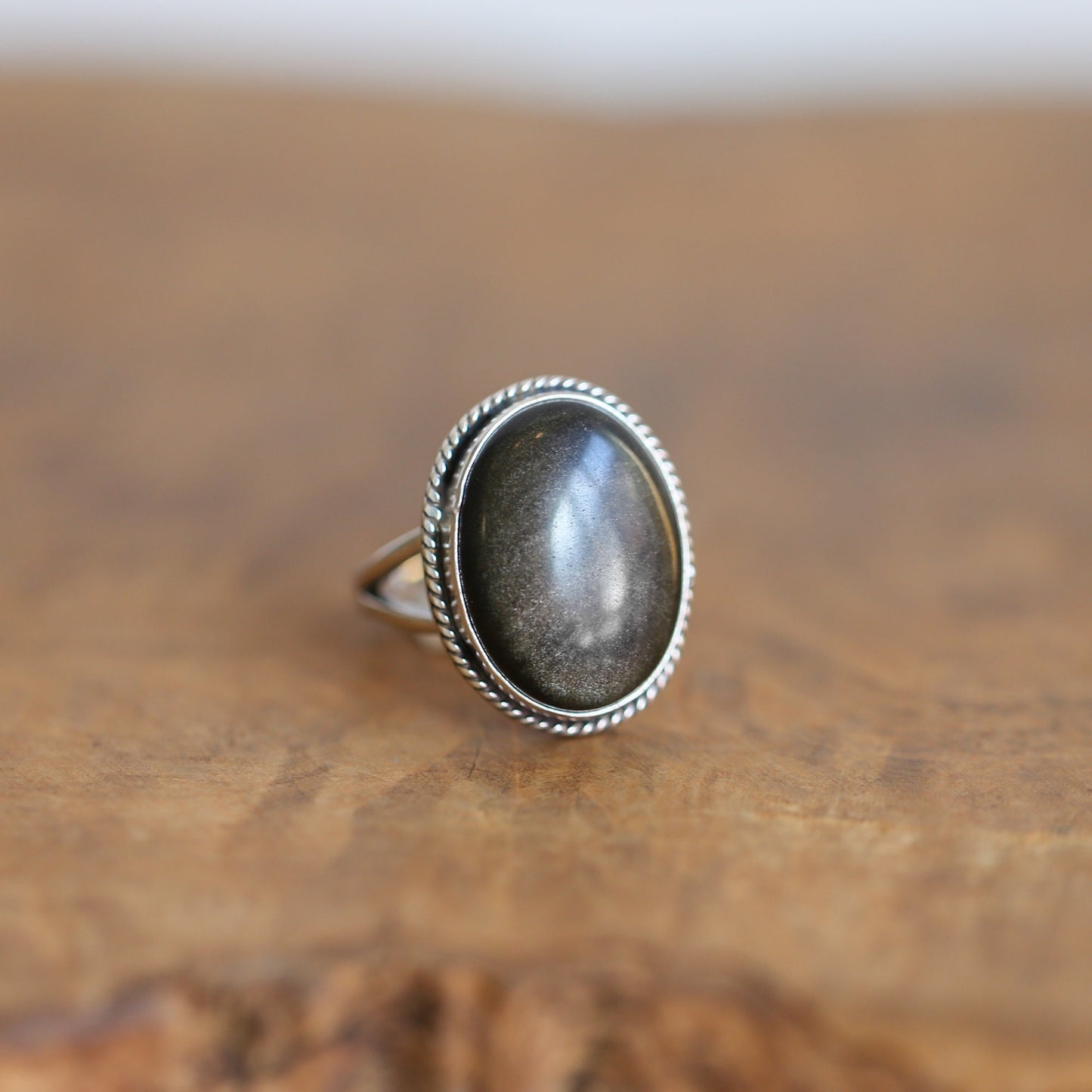 May include: A silver ring with an oval-shaped goldstone gemstone set in a rope-like border.