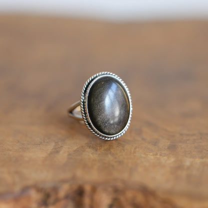 May include: A silver ring with an oval-shaped goldstone gemstone set in a rope-like border.
