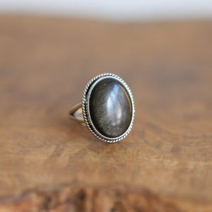 May include: A silver ring with an oval-shaped goldstone gemstone set in a rope-like border.