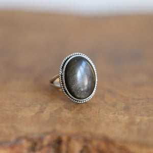 May include: A silver ring with an oval-shaped goldstone gemstone set in a rope-like border.
