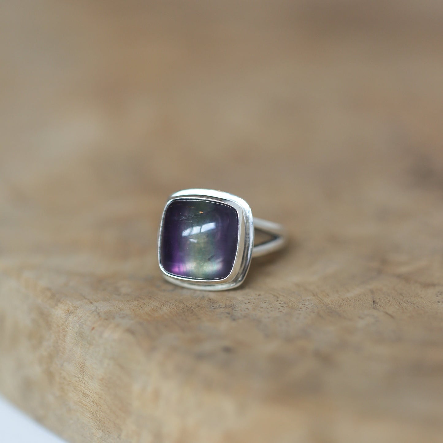 May include: A silver ring with a square-shaped, iridescent purple gemstone.