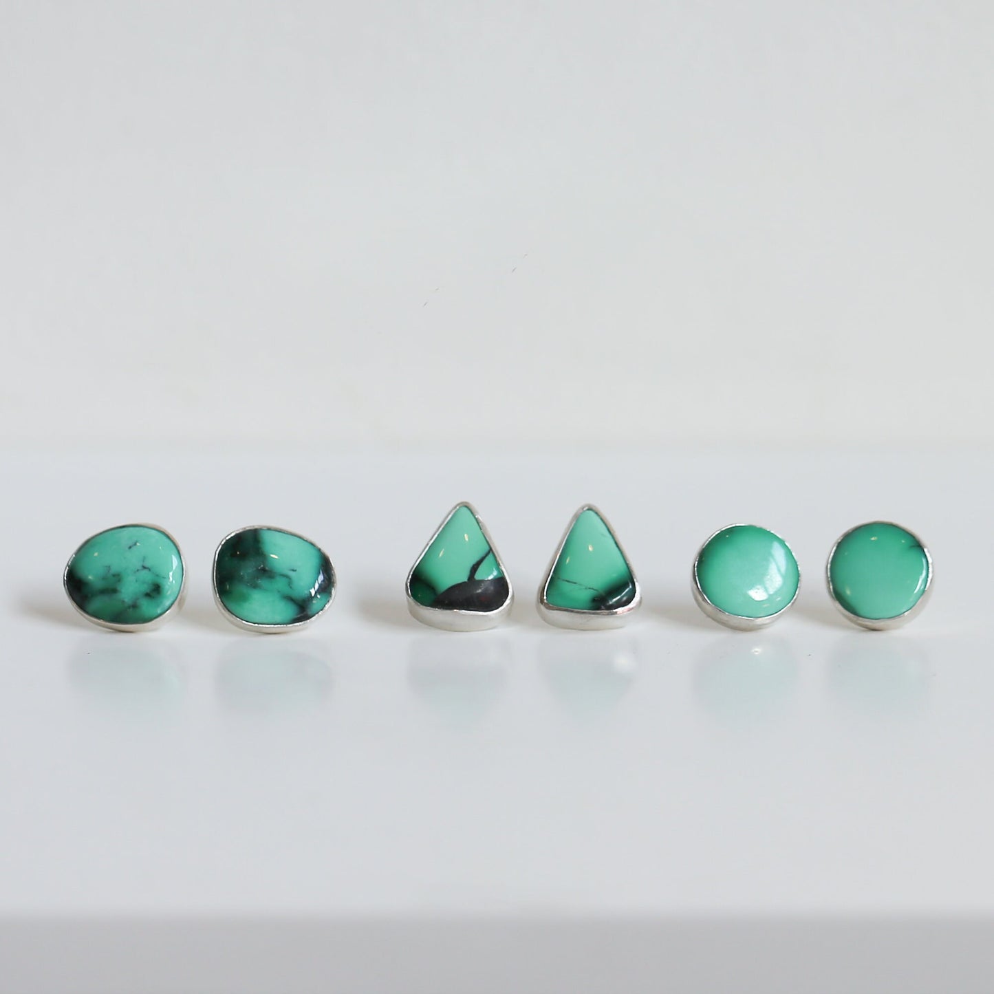 May include: A set of five turquoise earrings in different shapes, including round and triangular, with silver settings.