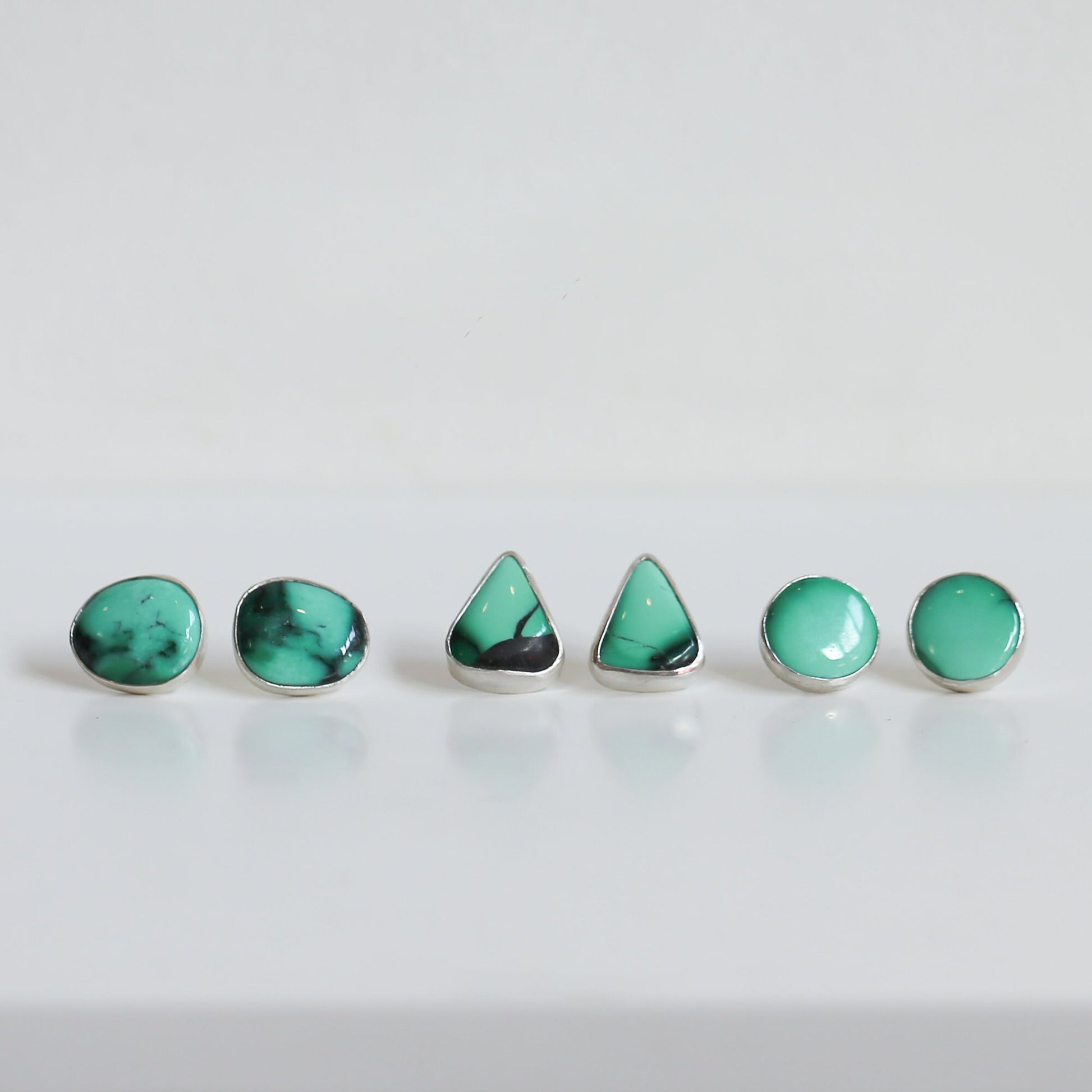 May include: A set of five turquoise earrings in different shapes, including round and triangular, with silver settings.