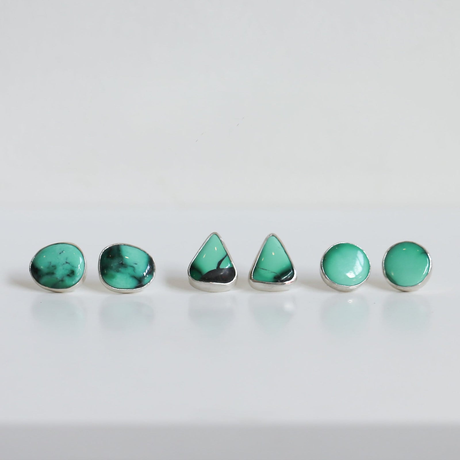 May include: A set of five turquoise earrings in different shapes, including round and triangular, with silver settings.