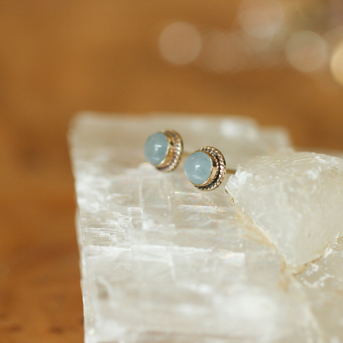 May include: A pair of aquamarine gemstone earrings with gold settings. The earrings are small and round, and the gemstones are a light blue color.