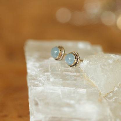 May include: A pair of aquamarine gemstone earrings with gold settings. The earrings are small and round, and the gemstones are a light blue color.