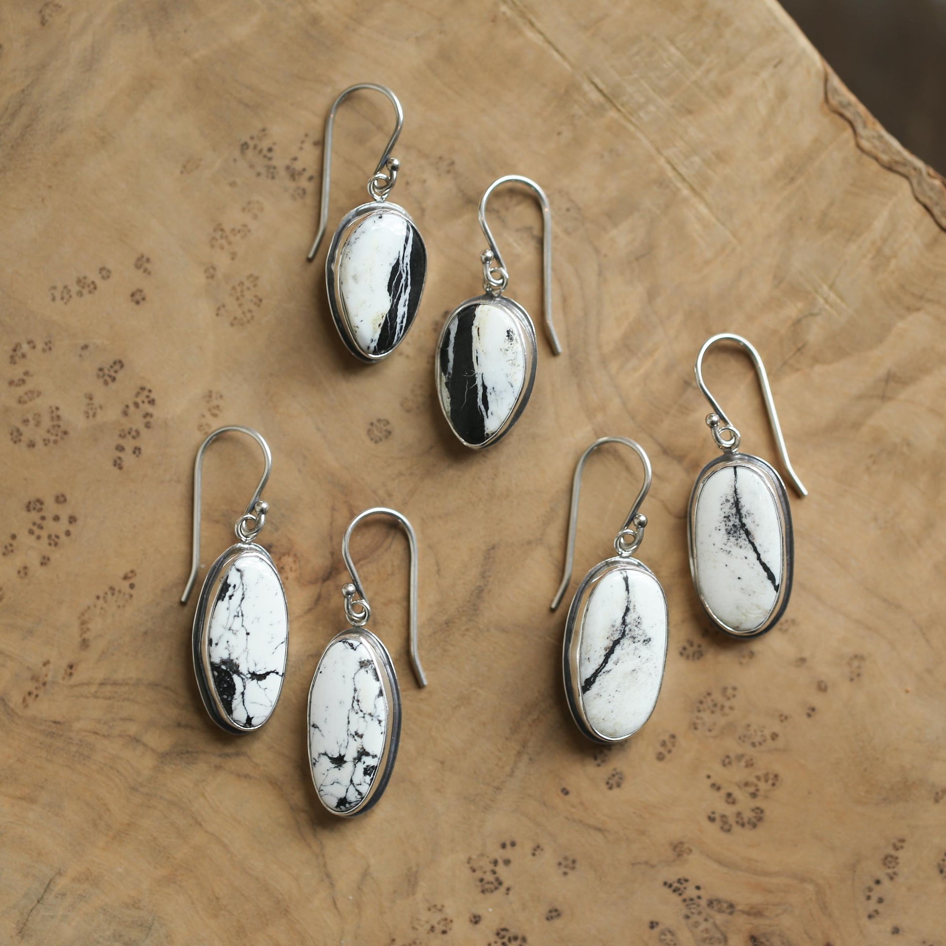 May include: Five pairs of silver dangle earrings with oval-shaped white and black stones. The stones have a natural, marbled pattern.