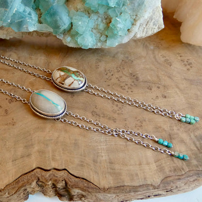 May include: Two silver bolo ties with oval-shaped stone pendants. One pendant has a turquoise stripe, the other has brown and green markings. Each tie has a chain and turquoise bead accents.