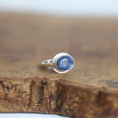 May include: A silver ring with a blue oval gemstone set in a bezel setting.