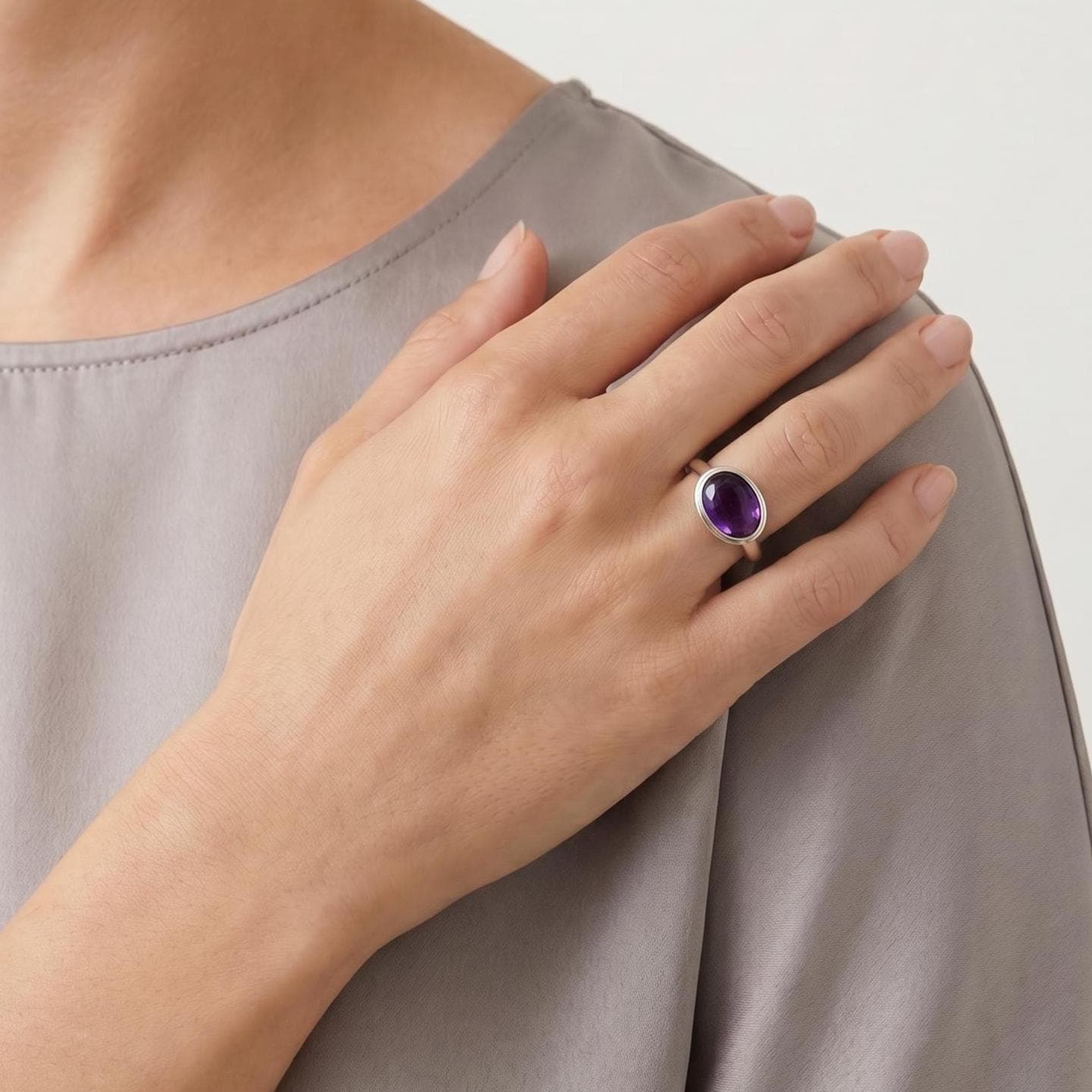 May include: A silver ring featuring a smooth, oval-shaped purple amethyst gemstone set in a polished metal band. The ring is worn on the ring finger, showcasing the deep violet color of the stone and the simple, clean design of the silver setting.