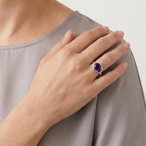 May include: A silver ring featuring a smooth, oval-shaped purple amethyst gemstone set in a polished metal band. The ring is worn on the ring finger, showcasing the deep violet color of the stone and the simple, clean design of the silver setting.