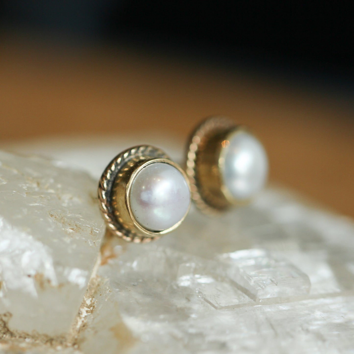 May include: A pair of gold pearl earrings with a textured gold band around the pearl.
