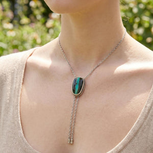 May include: Silver bolo tie with an oval turquoise and black stone pendant. The pendant is framed with a silver rope design. The bolo tie has a silver chain and decorative silver tips.