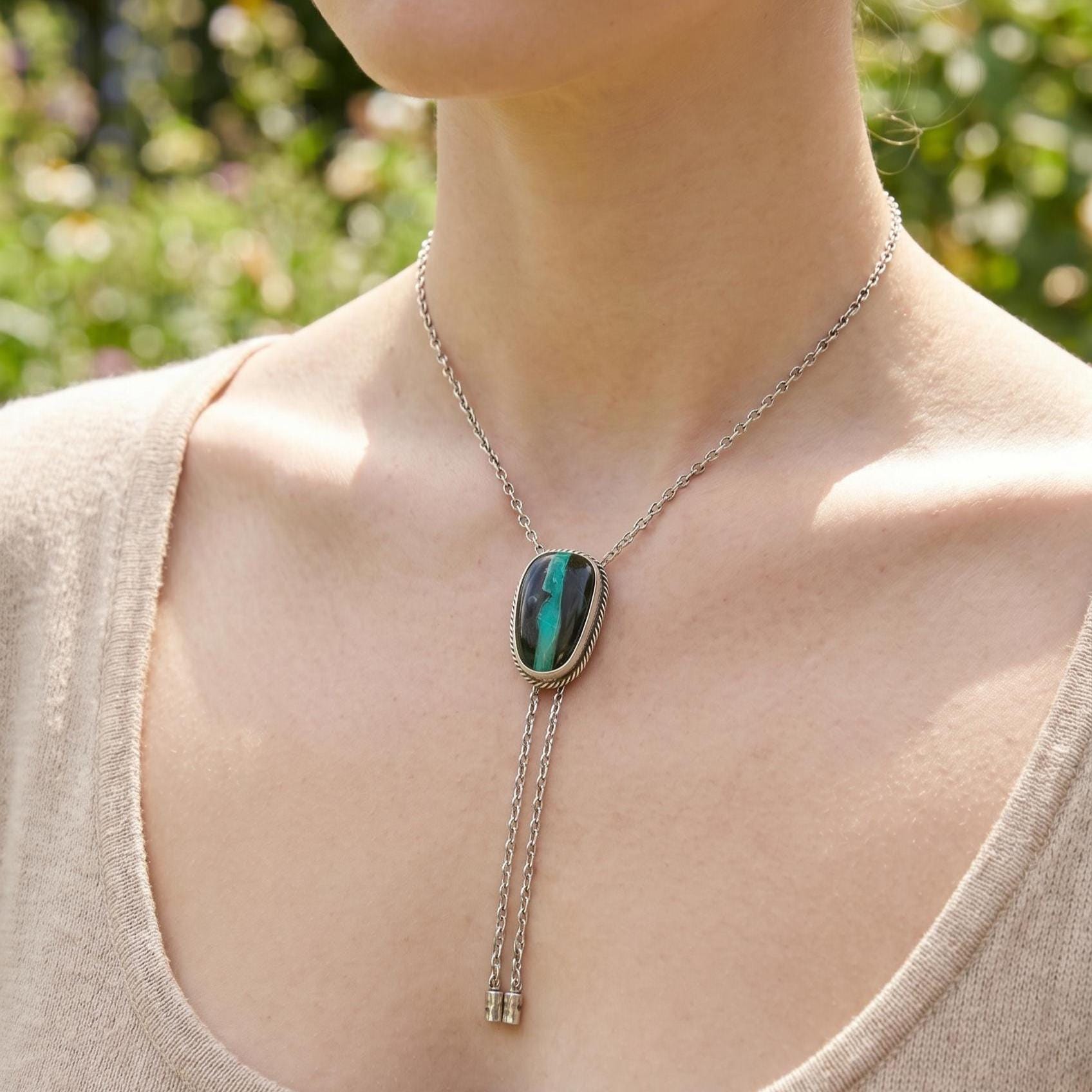 May include: Silver bolo tie with an oval turquoise and black stone pendant. The pendant is framed with a silver rope design. The bolo tie has a silver chain and decorative silver tips.